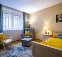 Ein Zimmer in einem Einfamilienhaus mit einem Bett, einem Sessel, einem Tisch und einem Boden in Holzoptik.