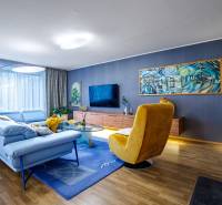 Wohnzimmer in einem Einfamilienhaus mit einem blauen Sofa, einem gelben Sessel und einem Boden in Holzoptik.