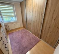 Ein Kleiderschrank mit Holzmuster, ein rosa Teppich, ein Fenster mit Jalousien in einer 4-Zimmer-Wohnung.