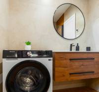 Badezimmer in einer Einzimmerwohnung mit Waschmaschine, rundem Spiegel und Schrank.