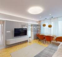 Obývací pokoj v 3-pokojovém bytě s televizí na stěně, pohovkou a jídelním stolem.