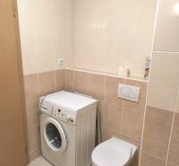 Badezimmer in einer 2-Zimmer-Wohnung mit hellen Fliesen, Waschmaschine und hängendem WC.