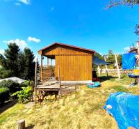 Eine Holzhütte in Partizánske, umgeben von Natur, mit einem grasbewachsenen Grundstück und einer Außensitzgelegenheit.
