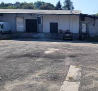 An der Straße Železničná befinden sich Lager und Hallen, ein Bereich mit Parkplätzen und Autos.