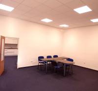 Ein Büro mit blauen Stühlen und Tischen, weiße Wand, offene Tür zu einer kleinen Küche.