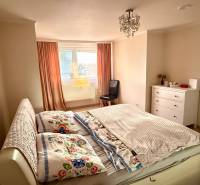 Schlafzimmer in einer 3-Zimmer-Wohnung mit Bett, Schrank und Fenster mit orangefarbenen Vorhängen.