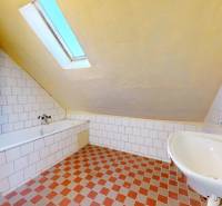 Ein Badezimmer in einem Einfamilienhaus mit Badewanne, Waschbecken und schräger Decke.