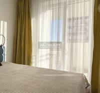 Helles Schlafzimmer in einer Einzimmerwohnung mit großem Fenster und Vorhängen.