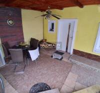 Die Terrasse des Einfamilienhauses mit Fliesen und Sitzmöbeln. In der Nische befinden sich ein Tisch und eine Uhr.