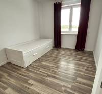 Ein Zimmer mit einem Bett, einem Boden in Holzoptik und einem großen Fenster in einer 3-Zimmer-Wohnung.