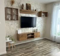 Wohnzimmer in einer 3-Zimmer-Wohnung mit Holzboden, einem aufgehängten Fernseher und Dekorationen.