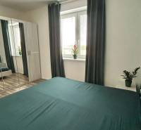 Schlafzimmer in einer 3-Zimmer-Wohnung mit einem Spiegelschrank, Vorhängen und einem Boden mit Holzdekor.