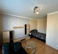 Ein Zimmer in einer Einzimmerwohnung mit einem Bett, einem schwarzen Sessel und einem Boden in Holzoptik.