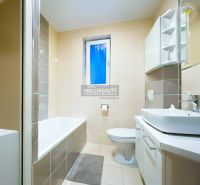 Badezimmer mit Badewanne und Waschbecken in einer 2-Zimmer-Wohnung, dominiert von hellen Fliesen.