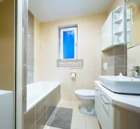 Badezimmer mit Badewanne und Waschbecken in einer 2-Zimmer-Wohnung, dominiert von hellen Fliesen.