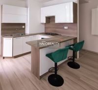 Küche in einer 2-Zimmer-Wohnung mit Bartresen, grünen Stühlen und Holzboden.