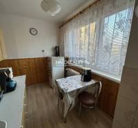 Küche mit Holzdekor in einer 2-Zimmer-Wohnung. Feine Vorhänge, Esstisch, Kaffeemaschine.