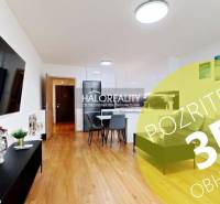 Wohnzimmer in einer Zweizimmerwohnung mit Holzboden, Essbereich und Fernseher an der Wand.