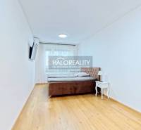 Helles Schlafzimmer mit Bett, Nachttisch und Fernseher in einer 2-Zimmer-Wohnung, Boden mit Holzdekor.