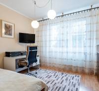 Ein Zimmer in einer 4-Zimmer-Wohnung mit einem Schreibtisch, einem Fernseher, einem Sessel und Vorhängen.