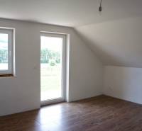 Helles Zimmer mit Fenstern, Holzboden und Glastüren in einem Einfamilienhaus.