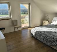 Helles Schlafzimmer in einem Einfamilienhaus mit Bett, Stuhl und Boden in Holzoptik.