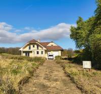 Ein Einfamilienhaus in Buková mit Zufahrtsstraße, Auto und umliegender Natur unter blauem Himmel.
