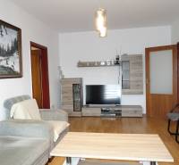 Wohnzimmer einer 3-Zimmer-Wohnung mit einem bequemen Sofa, Möbeln mit Holzdekor und einem Fernseher.