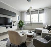 Wohnzimmer in einer 3-Zimmer-Wohnung mit großem Sofa, Fernseher, Teppich, Holzboden.