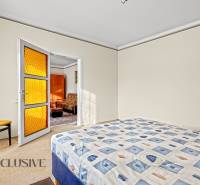 Schlafzimmer im Einfamilienhaus mit Bett, Sessel und Tür mit orangefarbenem Glas.