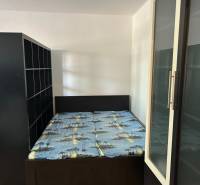 Ložnice v jednopokojovém bytě s postelí a úložnými skříňkami.