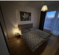 Schlafzimmer in einer 2-Zimmer-Wohnung mit Bett, Lampe, Bild und Boden mit Holzdekor.