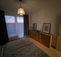 Schlafzimmer mit Kommode und Lampe, Boden mit Holzdekor in einer 2-Zimmer-Wohnung.