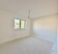 Ein geräumiges, helles Zimmer in einem Einfamilienhaus mit Doppelfenster und weißen Wänden.