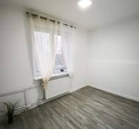 Ein Zimmer in einer 4-Zimmer-Wohnung mit einem Boden in Holzoptik, Vorhängen und einem Heizkörper.