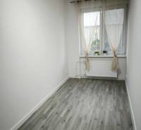 Ein kleiner Raum mit einem Holzboden, weißen Wänden und einem Fenster mit Vorhängen.