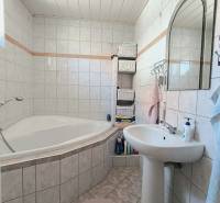 Ein Badezimmer in einem Einfamilienhaus mit einer Eckbadewanne, weißen Fliesen und Körben zur Aufbewahrung.