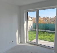 Innenraum eines Einfamilienhauses mit großem Fenster zum Garten, weiße Wände und Boden.