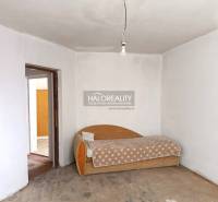 Innenraum eines Einfamilienhauses mit einem älteren Sofa und einem rohen Betonboden.