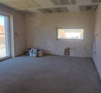 Ein Zimmer in einem Einfamilienhaus mit einem großen Fenster und einem einfachen Boden, wartet auf die Fertigstellung.