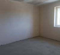 Ein leerer Raum mit Betonboden und einem großen Fenster in einem Einfamilienhaus.