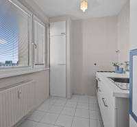 Küche in einer Einzimmerwohnung mit weißen Möbeln und Fliesen, mit Blick durch Jalousien.