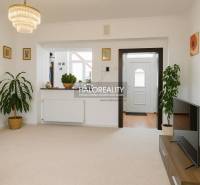 Wohnzimmer in einem Einfamilienhaus mit weißen Wänden, Blumen und einem Fernseher auf einem Tisch.