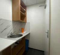 Kleine Küche mit Spüle, Regalen und einer orangefarbenen Kanne in Geschäftsräumen.