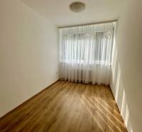 Ein Zimmer mit einem Holzboden in einer 3-Zimmer-Wohnung, Vorhänge am Fenster.