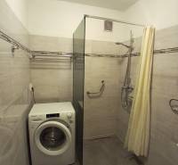 Badezimmer mit Dusche, Waschmaschine und hellen Fliesen in einer 3-Zimmer-Wohnung.