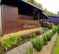 Eine Holzhütte in den Gärten in Bytča, umgeben von gepflegtem Grün und einem Weg aus Fliesen.