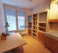 Ein Arbeitszimmer in einer 2-Zimmer-Wohnung mit einem Holzboden, einem Tisch und einem Bücherregal.