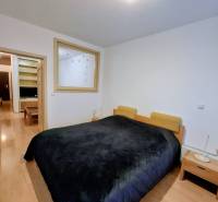 Schlafzimmer mit breitem Bett, Nachttischen und Holzboden in einer Zweizimmerwohnung.