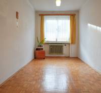 Ein Zimmer in einem Einfamilienhaus mit einem Boden in Holzoptik, einem Heizkörper und einem Fenster mit Gardine.